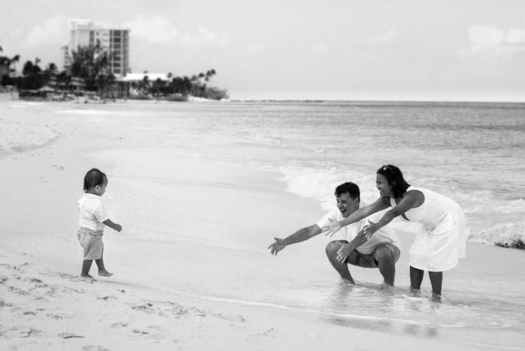 A child on the beach walking toward two adults reaching out with open arms
